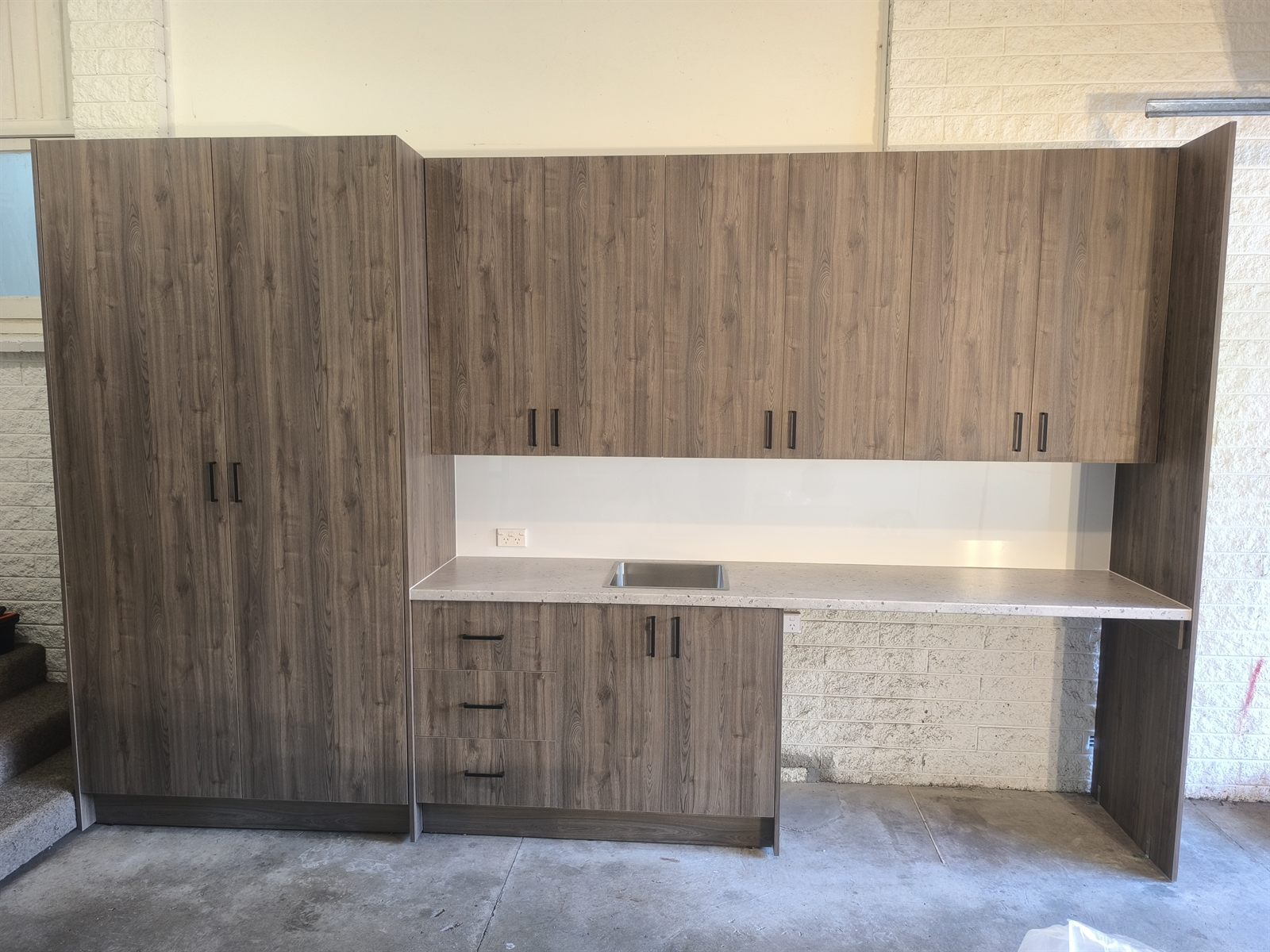 Finished laundry storage cabinetry with tall cupboards, drawers, bench space and sink